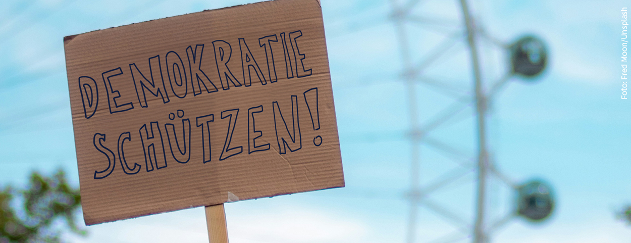 Auf dem Bild ist ein Pappplakat mit der Aufschrift "DEMORATIE SCHÜTZEN".