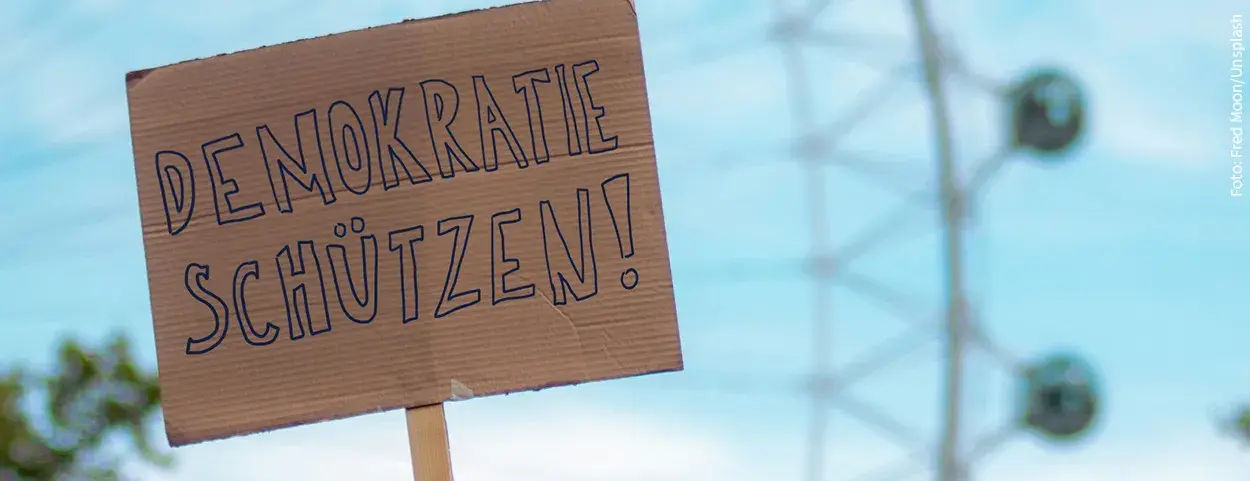 Auf dem Bild ist ein Pappplakat mit der Aufschrift "DEMORATIE SCHÜTZEN".