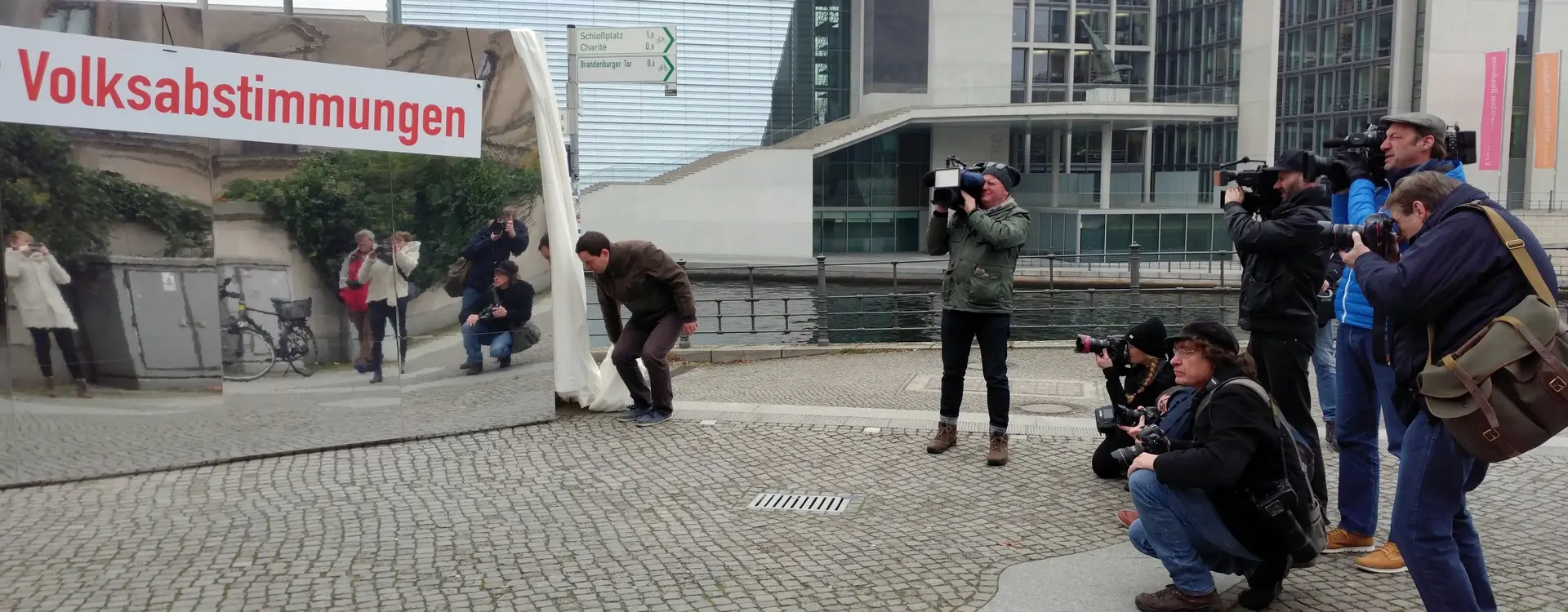Auf dem Bild sind vier Fotografen und und drei Kameramänner, die einen Spiegel, welcher "Volksabstimmungen" zeigt festhalten.