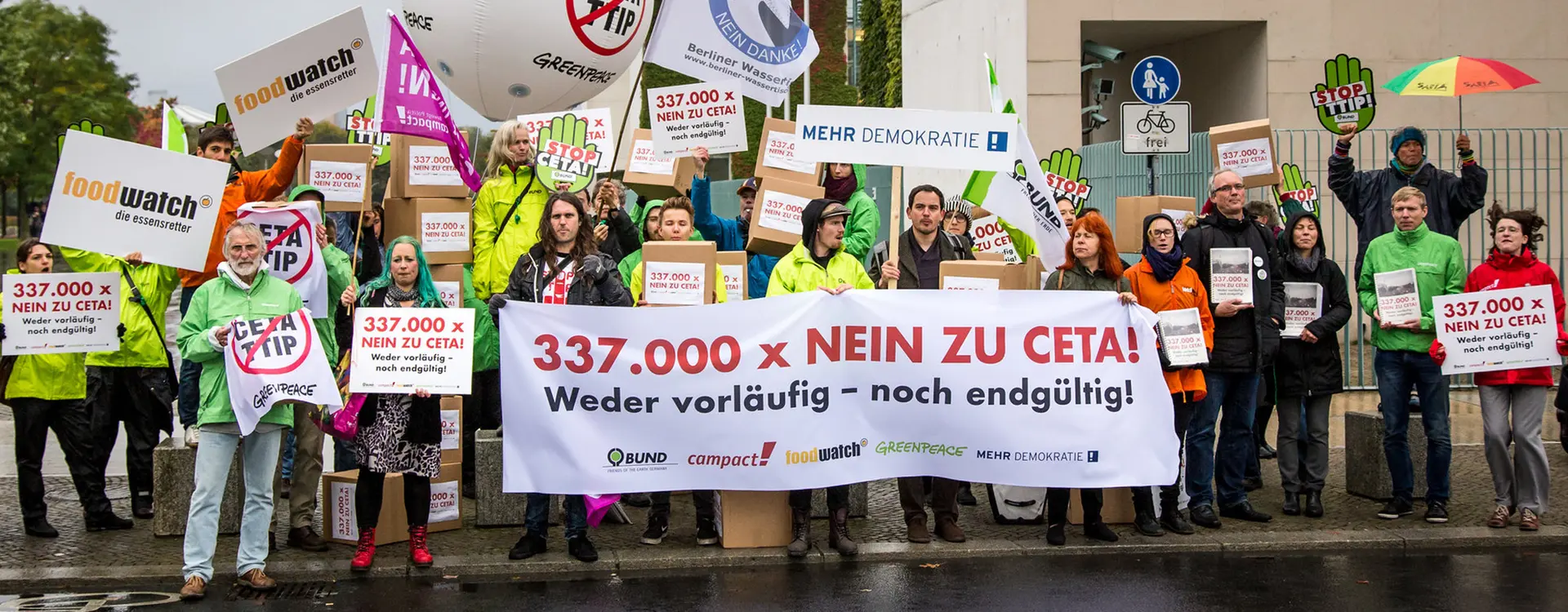 Auf dem Bild ist eine Protest Aktion von Mehr Demokratie, Compact!, Greenpeace und weiteren Organisationen. es wird ein Transparent hochgehalten mit der Aufschrift: 337.000 x NEIN ZU CETA!, Absatz Weder vorläufig - noch endgültig.