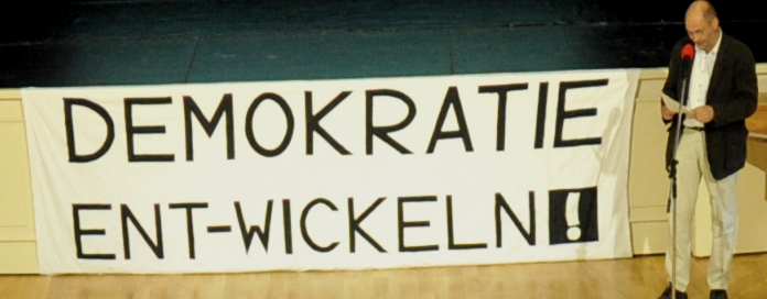 In einem Klassenraum ist ein Transparent mit dem Text "DEMOKRATIE ENT-WICKELN!".
