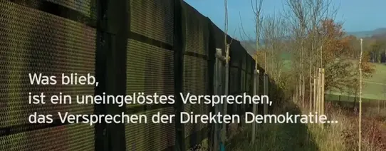 runder tisch Auf dem Bild sieht man eine Lärmschutzwand und dahinter junge Bäume, welche wachsen. Darüber ist der Text "Was blieb, ist ein uneingelöstes Versprechen, das Versprechen der Direkten Demokratie...".