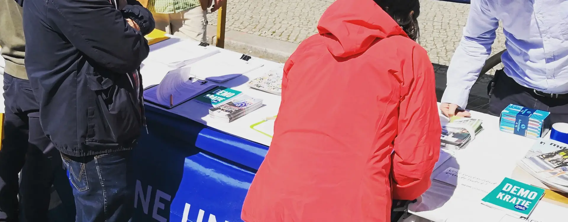 Zu sehen ist ein Informationsstand von Mehr Demokratie und interessierten Menschen davor.