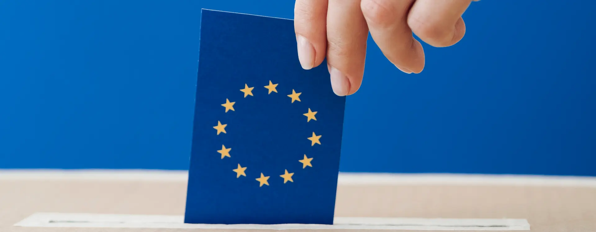 Auf dem Bild wird in eine Wahlurne ein Umschlag mit EU Flagge eingeworfen.