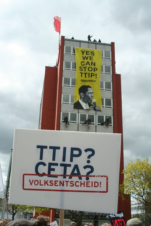 An einem Hochhaus hängt ein Transparent herunter, mit dem Text "YES WE CAN STOP TTIP!".