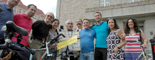 10 Personen stehen mit Fahrrädern vor einem Gebäude und gucken in die Kamera.