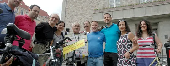 10 Personen stehen mit Fahrrädern vor einem Gebäude und gucken in die Kamera.