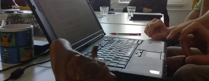 Auf dem Bild ist ein Laptop im Fokus, in einer Besprechung im Tischkreis.