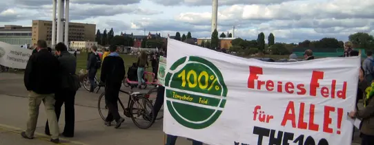 (Aktion gegen Bebauung des Tempelhofer Feldes | Quelle: http://www.thf100.de) Auf dem Protestmarsch wird ein Transparent gehalten, mit der Aufschrift "100% Tempelhofer Feld" und "Freies Feld für ALLE! www.THF100.de".