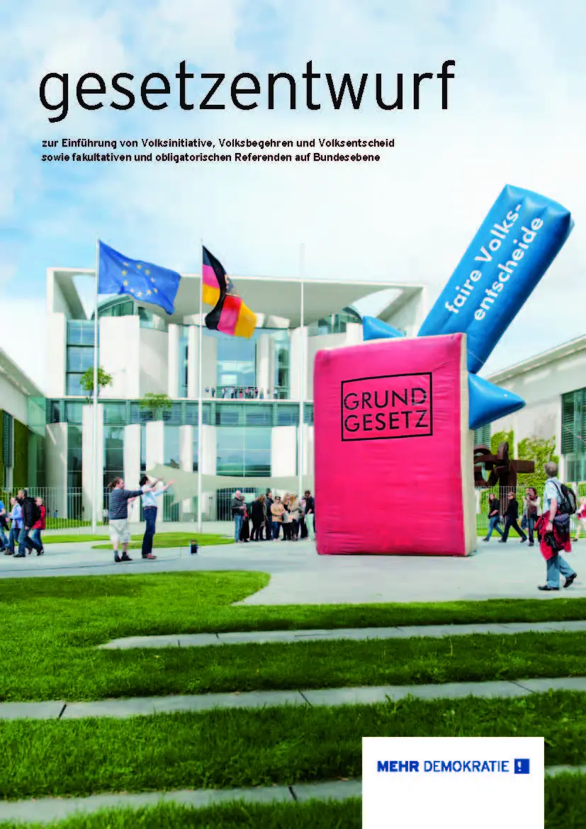 Es ist das Kanzleramt zu sehen, davor ist ein circa fünf mal fünf hohes aus Plastik und aufgeblasenes Grundgesetz mit einem ebenfalls aus Plastik und aufgeblasenem Pfeil, wodrauf steht "faire Volksentscheide".