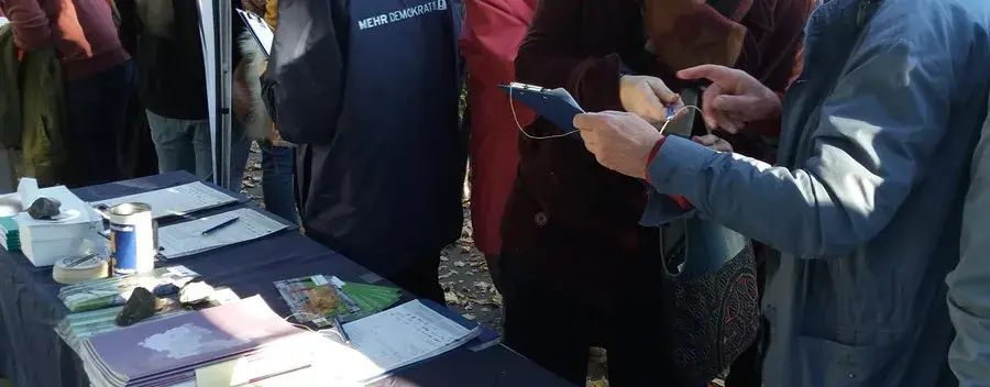 Auf dem Bild sind sehr viele Menschen vor einem Informationsstand von mehr Demokratie.