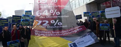 Ein Protest auf dem Foto ist zu sehen und in der Mitte ist ein riesiges Transparent, welches die Aussage trifft "72% der Deutschen wollen Bundesweite Volksabstimmungen".