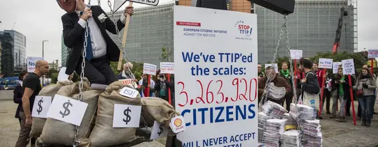 Es ist eine altertümliche Waage zu sehen, auf der rechten Seite ist Papier und auf der linken Seite mein Mensch mit ganz vielen Geldsäcken. In der Mitte steht ein Schild, mit dem Text "We've TTIP'ed the scales: 3.263.920 Citizens will never accept TTIP & CETA!".
