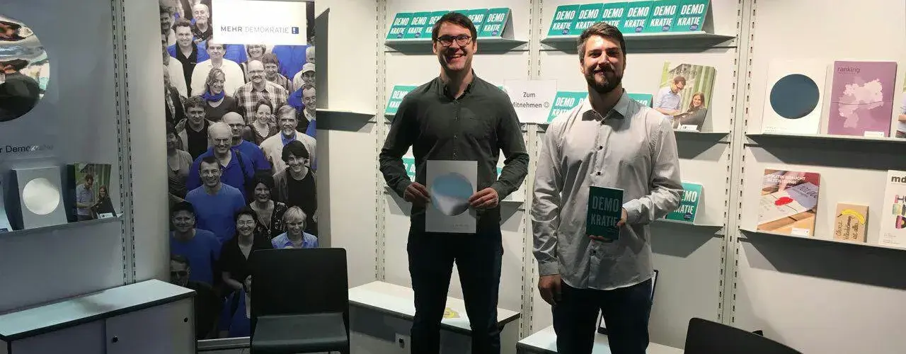 Zwei Menschen stehen an einem Informationsstand von Mehr Demokratie.