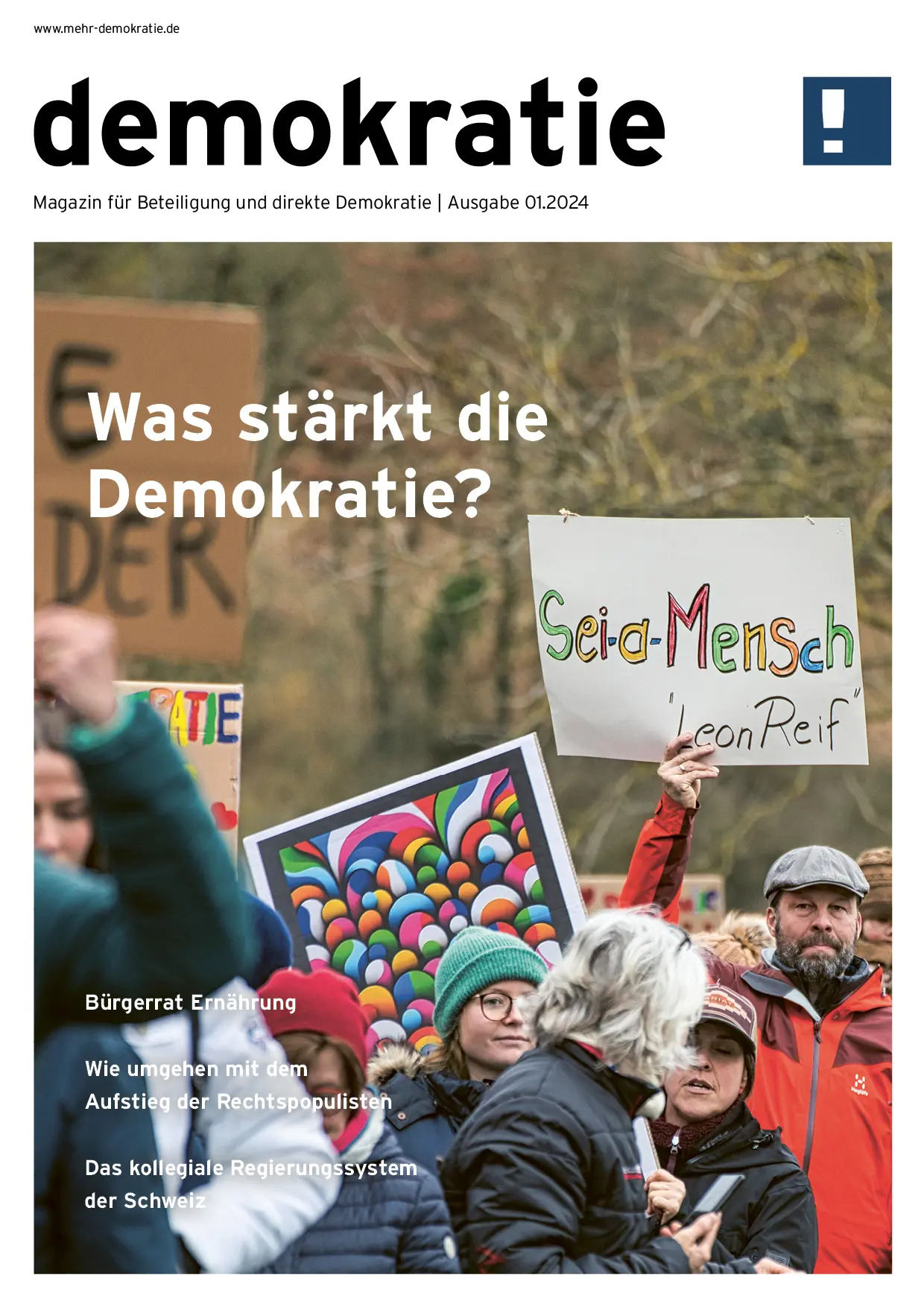 Zu sehen ist das Deckblatt von der Magazin Ausgabe vom 01.2024. Zu sehen ist ein Protestmarsch, wo ein Mann ins Auge fällt, der der Schild hochhält mit den Worten: Sei-d-Mensch ´Leon Reif´. Links-oben im Vordergrund steht: Was stärkt die, Absatz Demokratie.