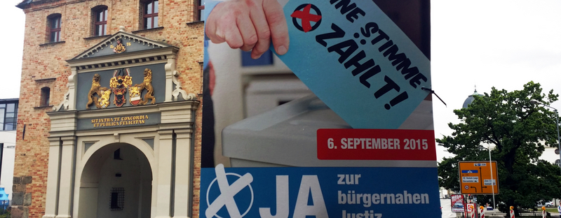(Steintor in Rostock | Foto by Charlie Rutz | Lizenz: CC BY-SA 2.0) Ein Plakat an einer Laterne ruft zum Volksentscheid auf.