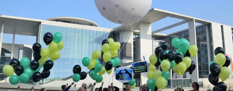 In Berlin stehen Menschen vor der Spree mit einem Luftballon, der die Aufschrift "Volksabstimmung" hat.