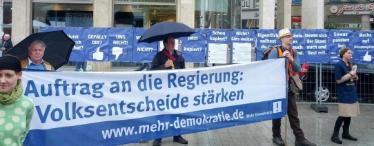 Fünf Menschen sind bei einer Protestaktion und halten ein Transparent, mit der Aufschrift "Auftrag an die Regierung: Volksentscheide stärken".