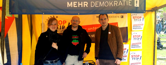 (Anti-TTIP-Aktion beim MyFest in Berlin am 1. Mai 2015 | v.l.: Regine Laroche, Dr. Michael Efler, Charlie Rutz | Foto by Kurt Wilhelmi | CC BY-SA 2.0) Ein Infostand von Mehr Demokratie gegen TTIP.