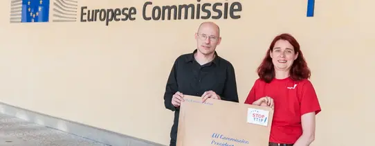 Vor dem Gebäude der Europäischen Kommission stehen zwei Menschen mit einem übergroßen Brief und einer imaginären Briefmarke, wo "STOP TTIP!" drauf steht.