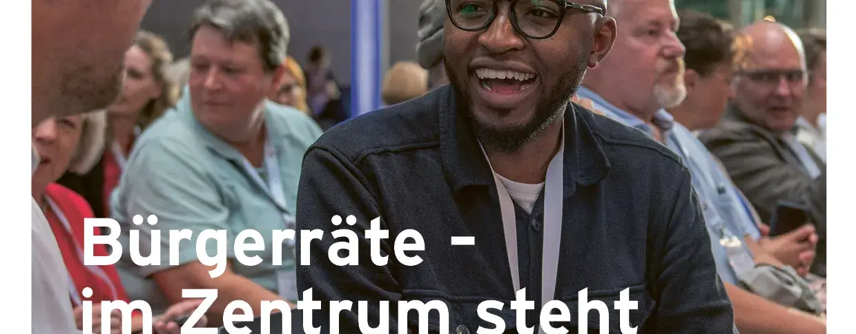 Zu sehen ist das Deckblatt von der Magazin Ausgabe vom 04.2023. Auf dem Bild sind zwei Menschen im Fokus, welche sich unterhalten und dabei fröhlich sind und im Hintergrund ebenfalls Menschen sind, die sich unterhalten. Links-mittig steht im Vordergrund: Bürgerräte - im Zentrum steht das Gespräch.