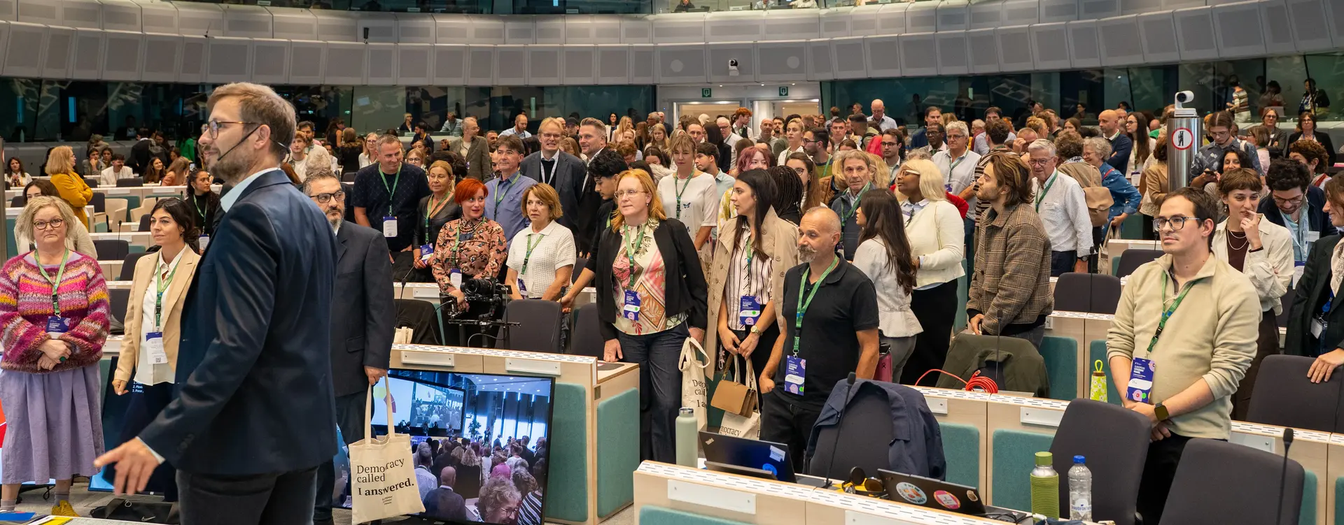 Teilnehmerinnen und Teilnehmer des EU-Bürgerforums zur demokratischen Widerstandsfähigkeit versammeln sich in einem großen Sitzungssaal. Menschen unterschiedlichen Alters und unterschiedlicher Herkunft stehen zwischen den Sitzreihen und kommen miteinander ins Gespräc