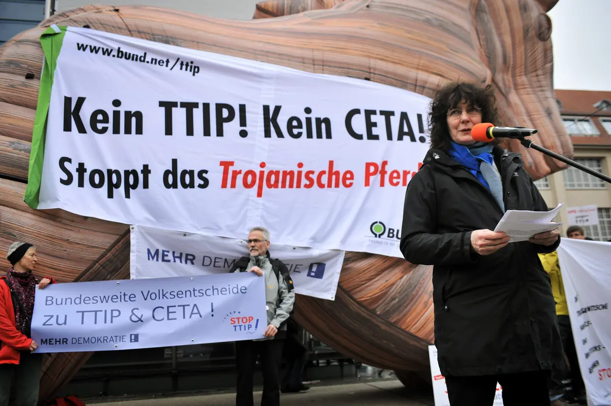 Eine Frau hält vor dem trojanischen Pferd eine Rede.