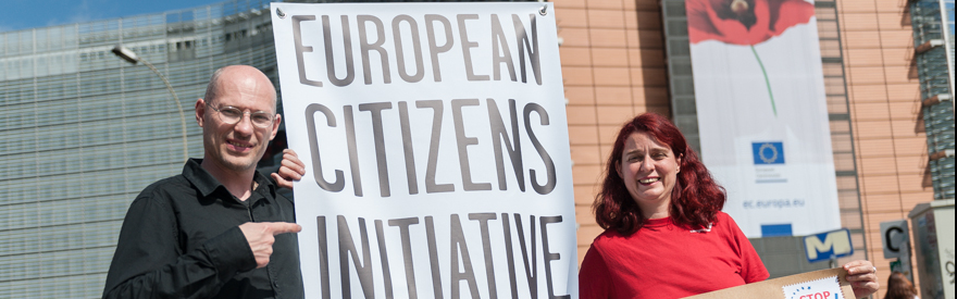Auf dem Bild sind zwei Personen im Fokus, mit der Aufschrift "European Citizens Initiative" auf einem Transparent.
